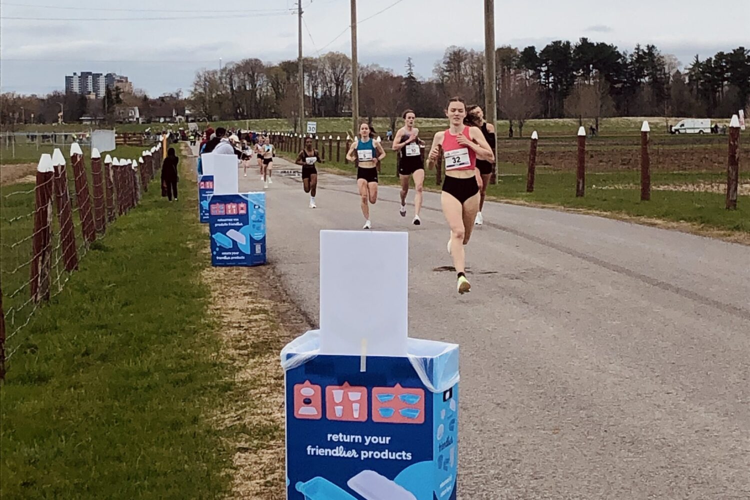 Blue boxy return bins alongside an Ottawa pathway. Participants run in the background.