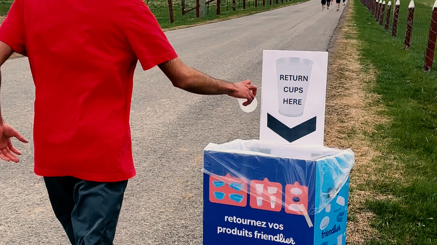 A runner drops a reusable cups into a bin marked "Return cups here". Photo by Craig Conoley/EnviroCentre.