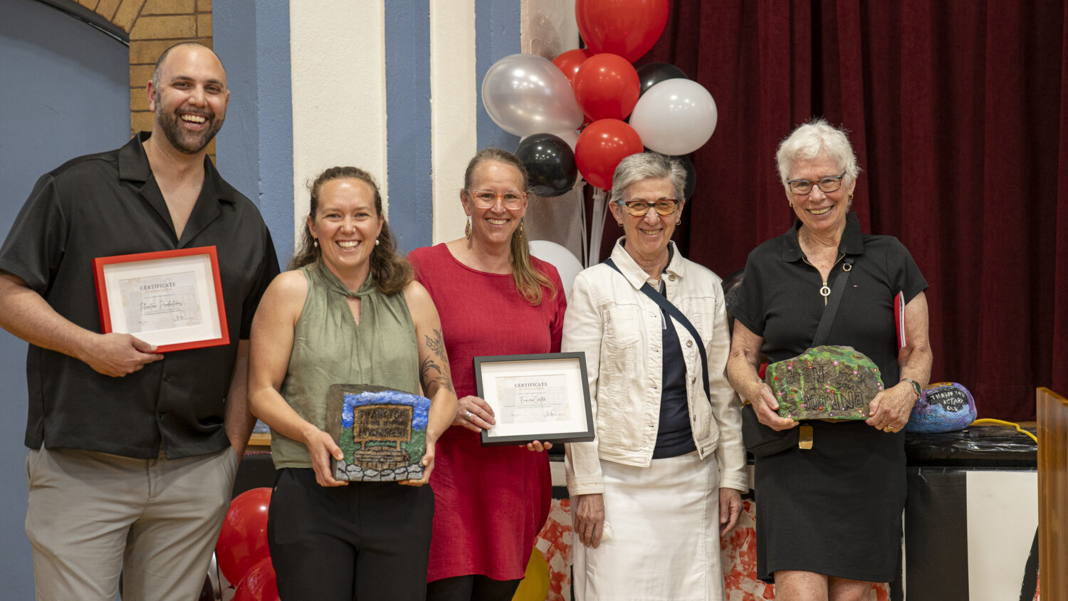 Project partners pose for a photo, each holding either a large painted rock of a certificate of appreciation.