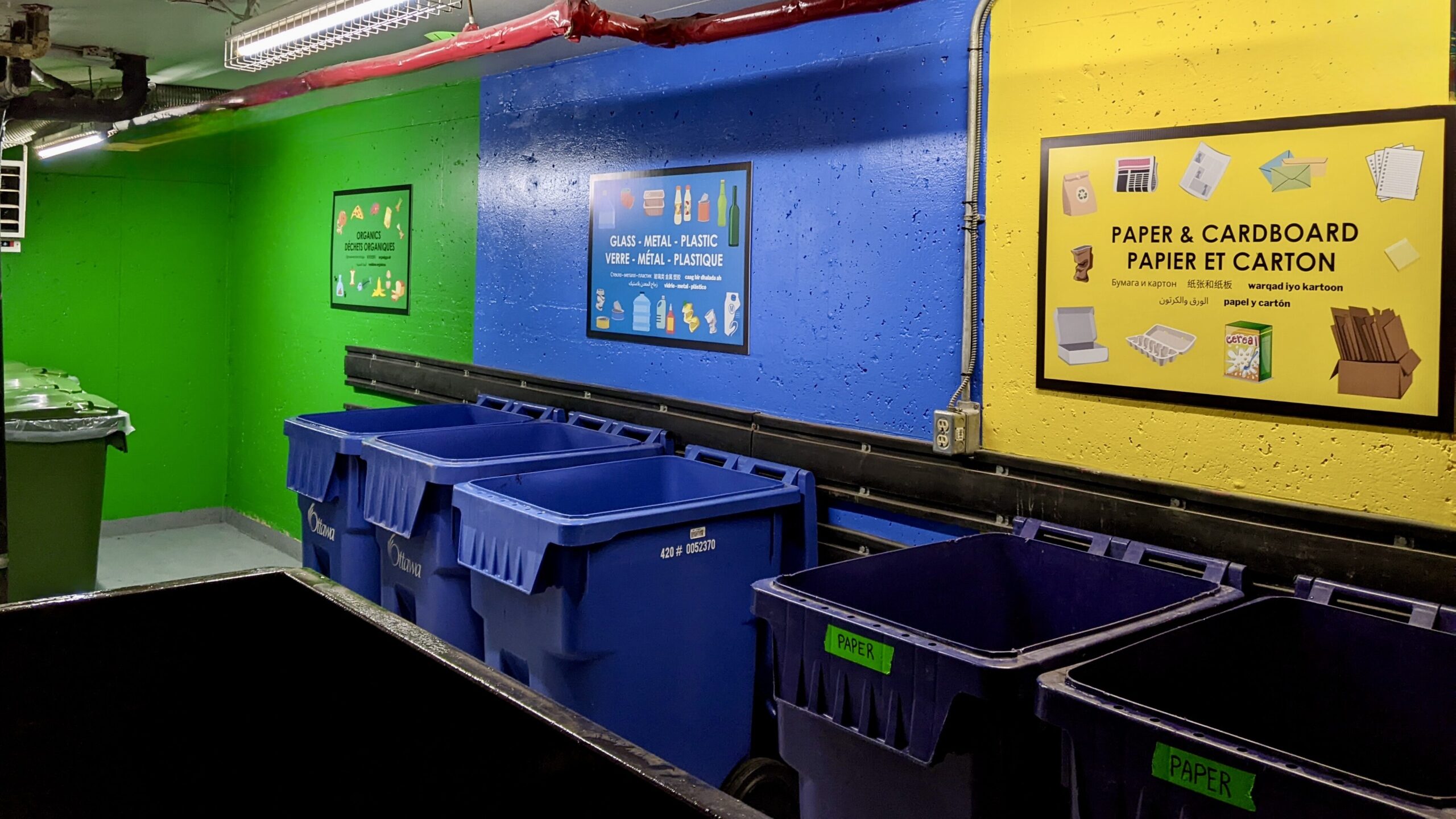 The polished waste room of a residential high rise in Ottawa. The walls are painted in green, blue and yellow sections.